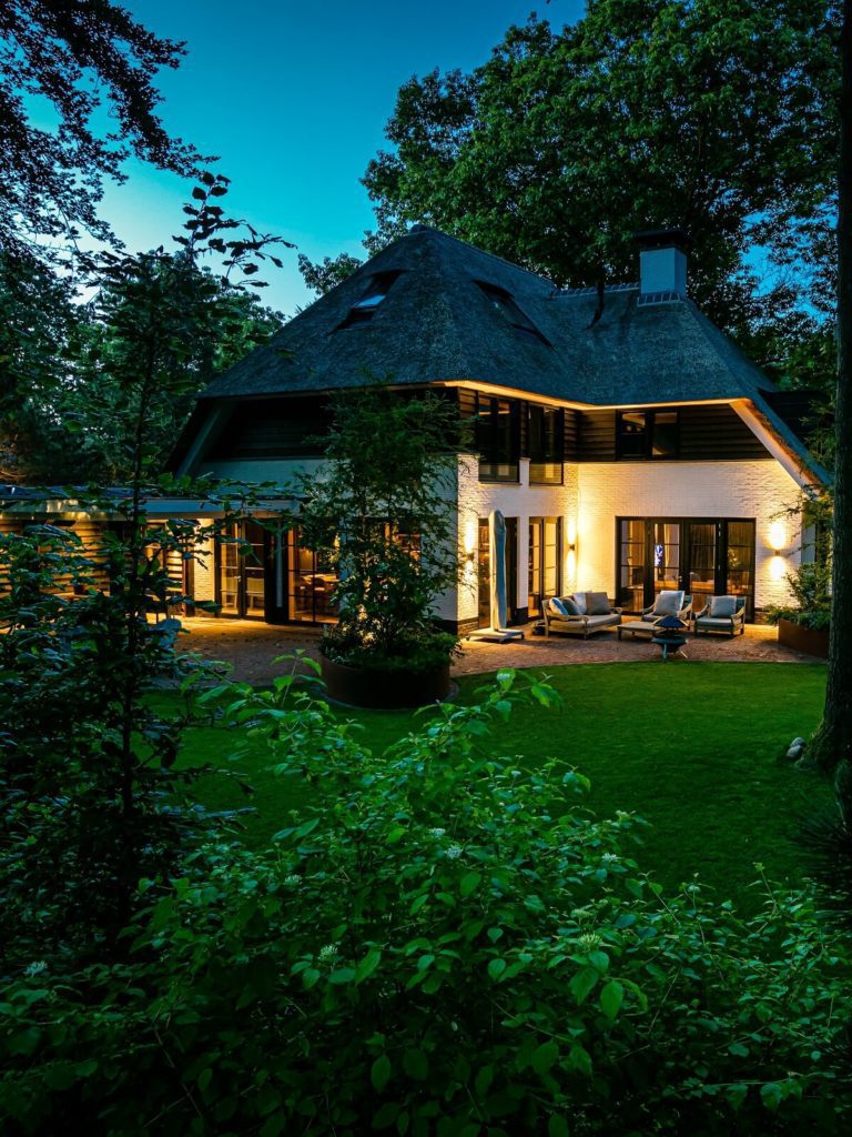 Achterzijde zicht vanuit de tuin in de avond rietgedekte villa gebouwd door Lichtenberg Exclusieve Villabouw.