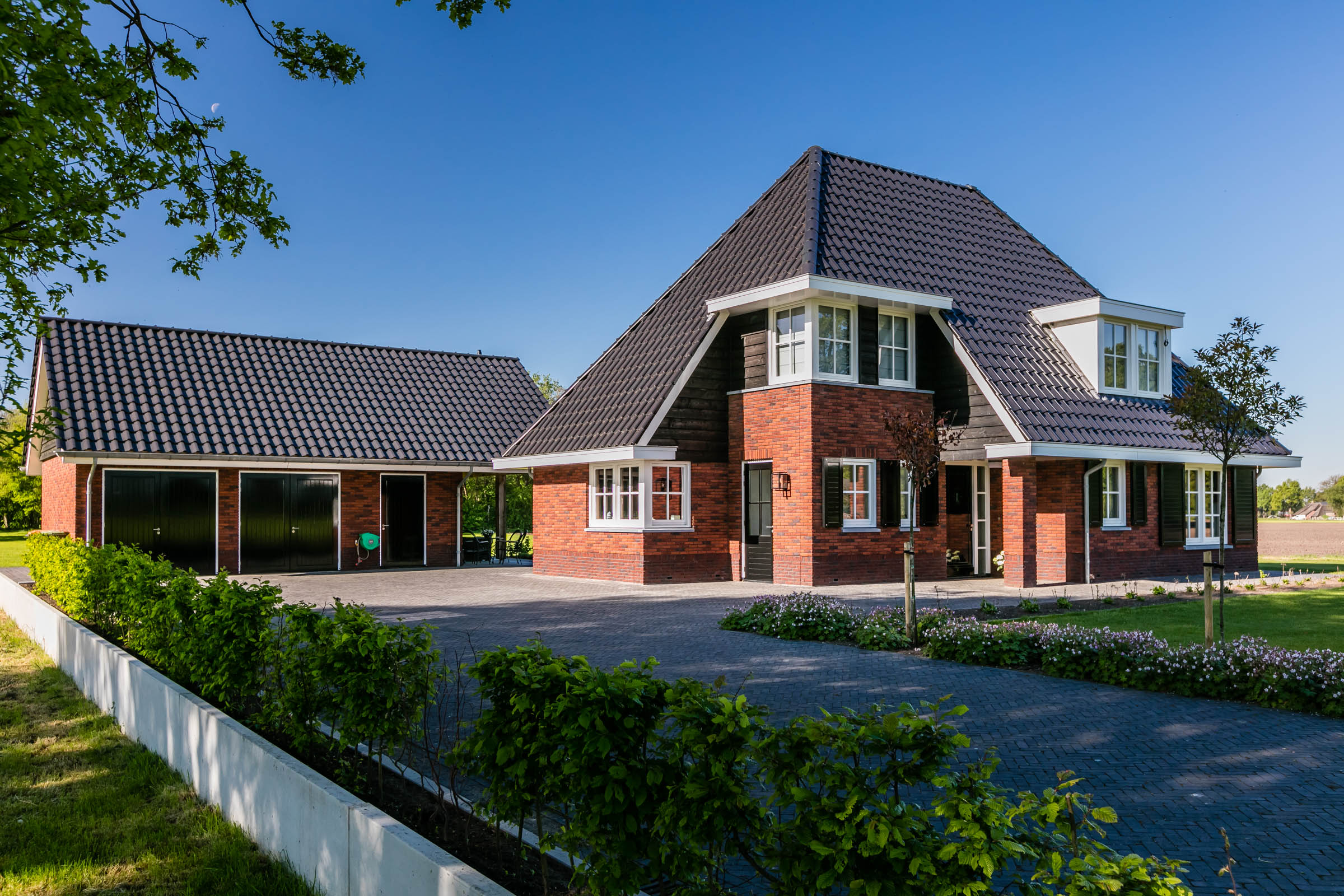 Voorgevel en bijgebouw met dubbele garage bij landelijke villa in Twente.